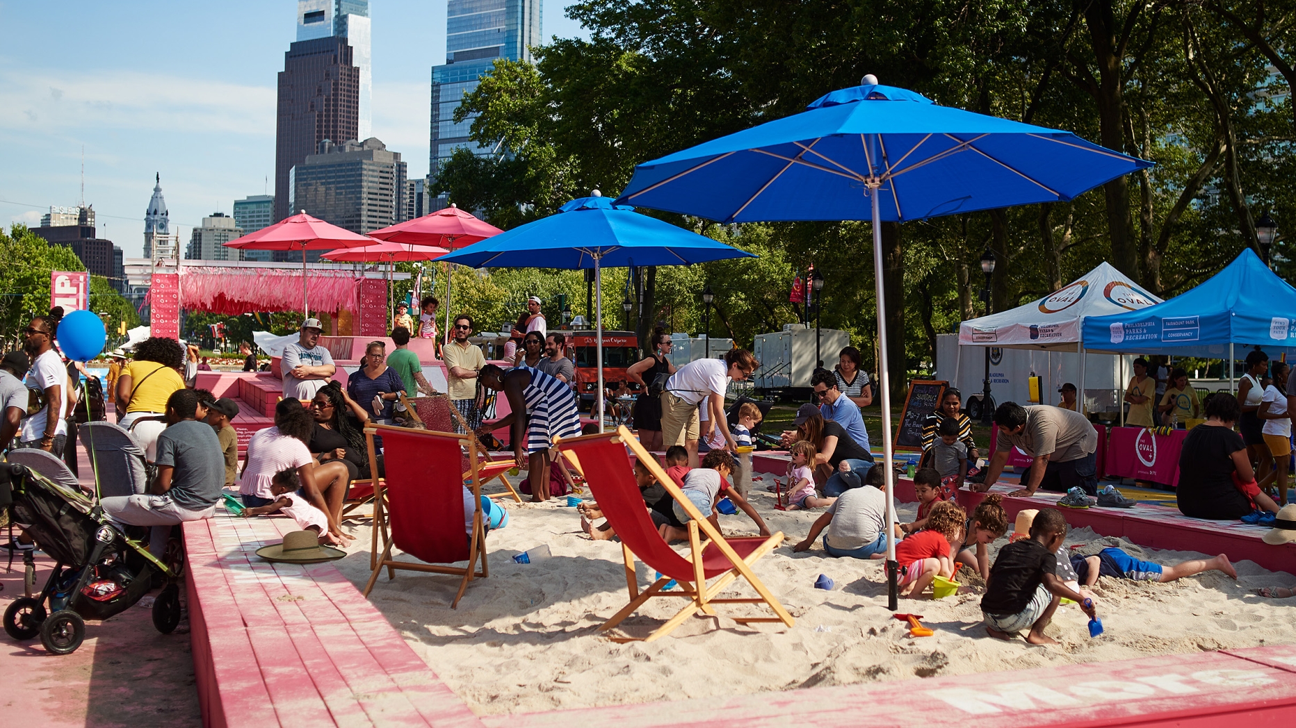 Sand box with beach chairs, parasol and people hanging out. Philadelphia skyline in background