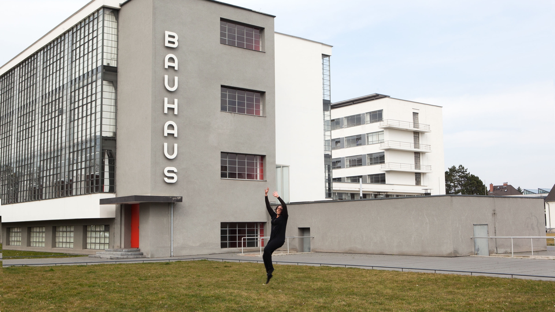 Student dancing on lawn in front of building with large sign saying "Bauhaus".
