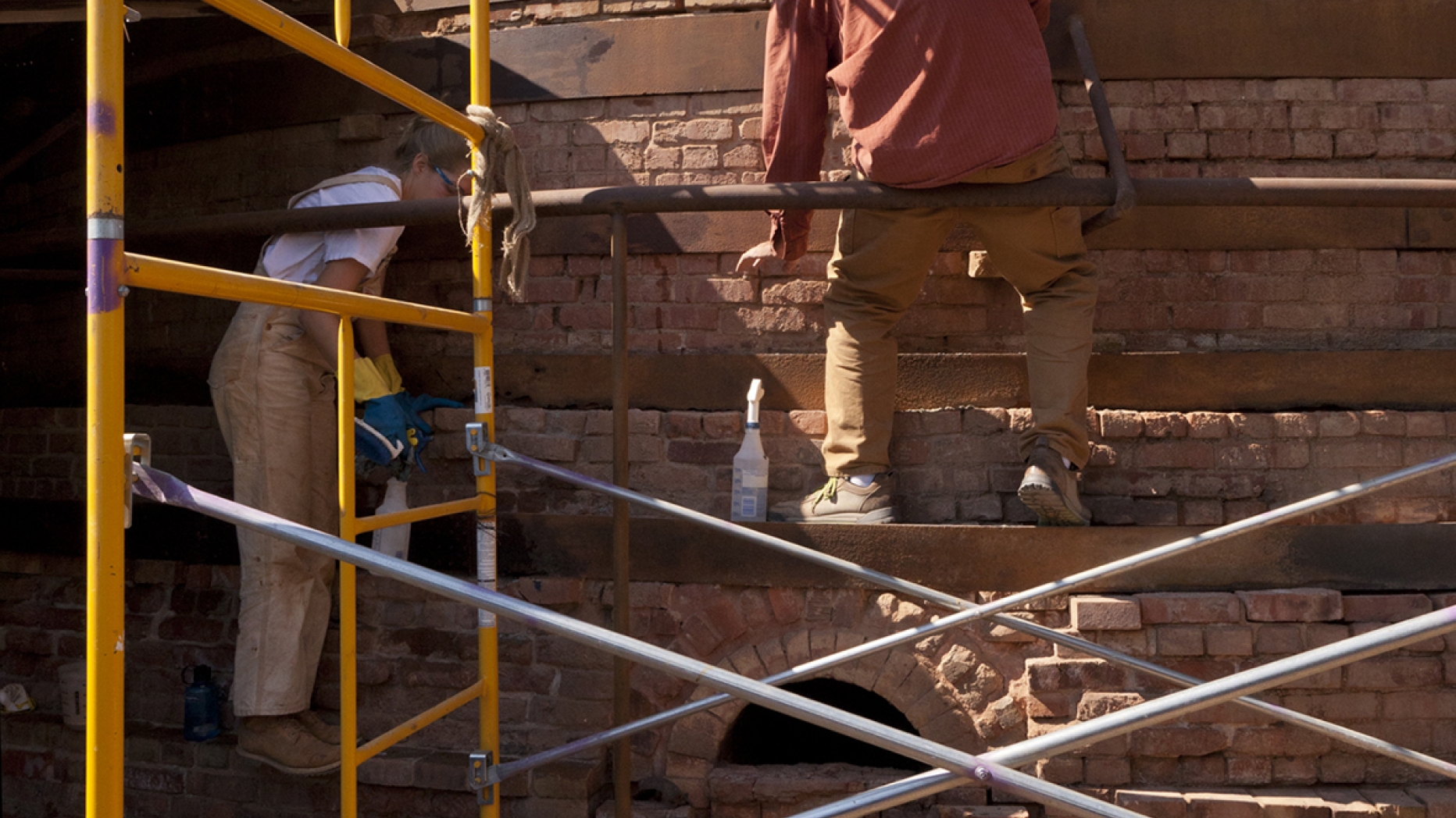 People sitting of scaffolding working on a structure made of bricks.