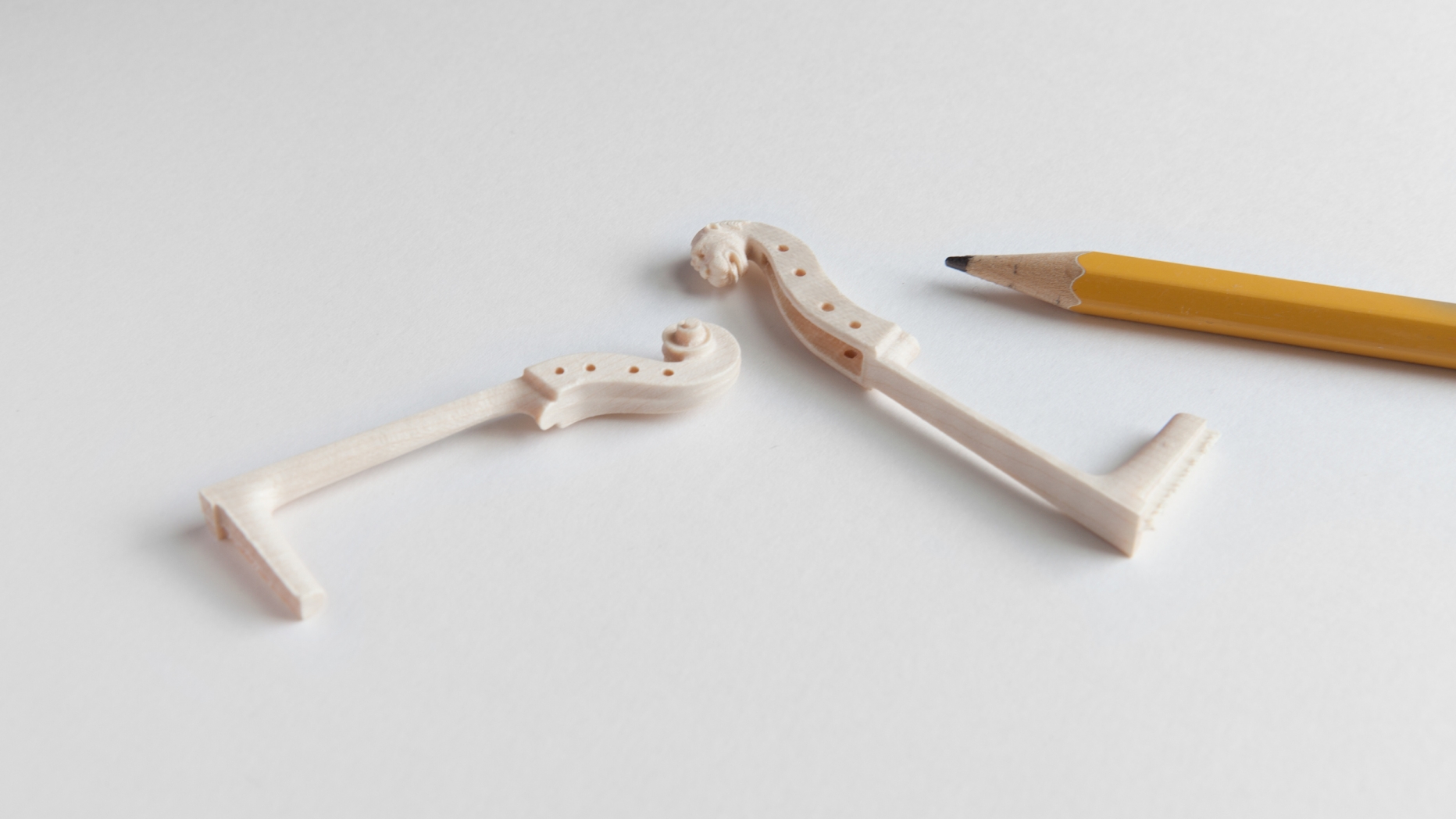 Miniature cello and viol necks next to pencil for comparison
