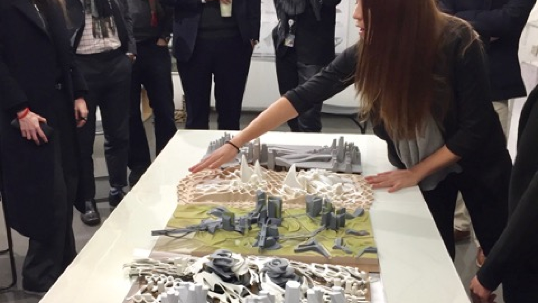 Student showing work to a group that resembles a series of architectural models.