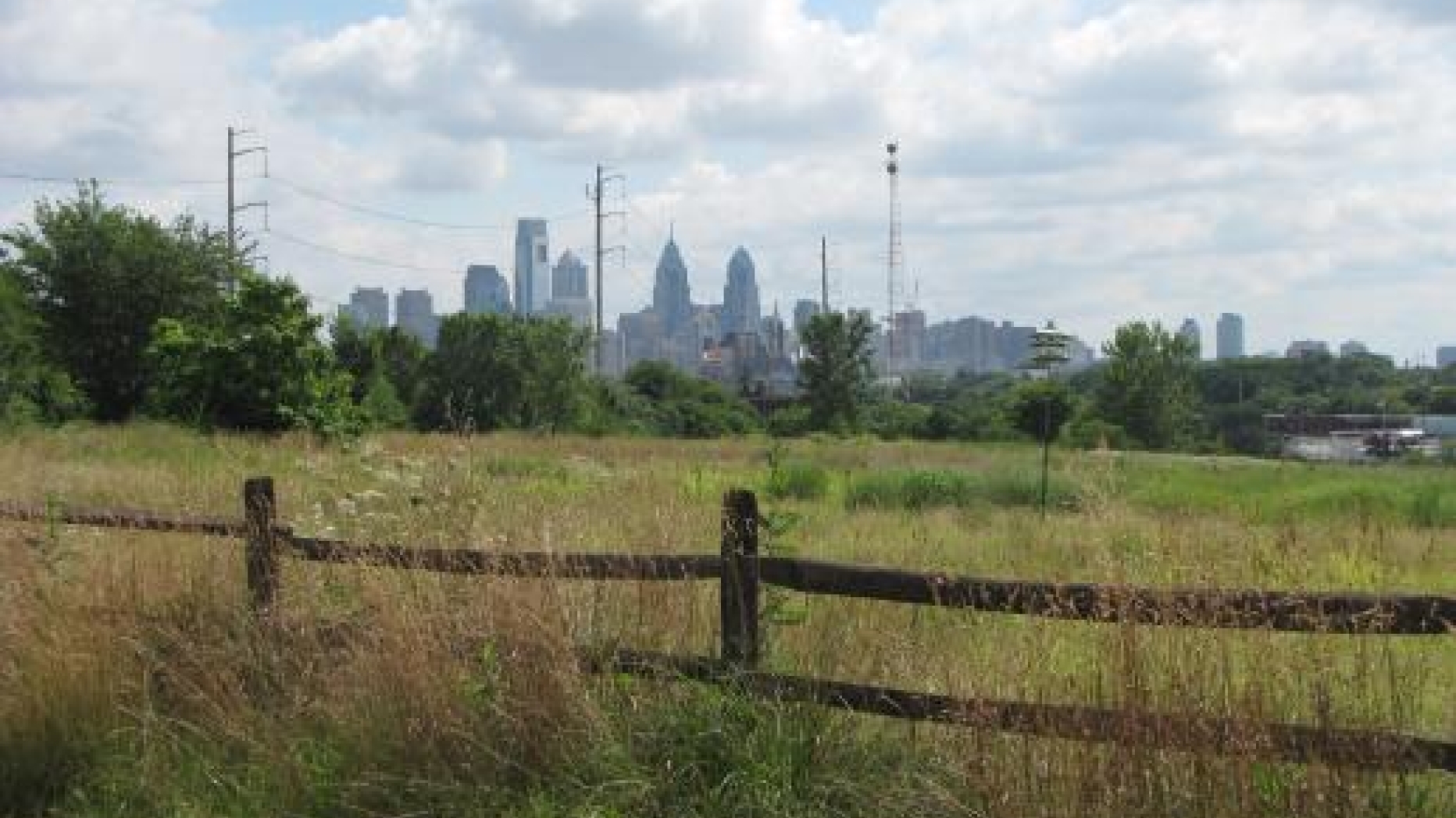 A fenced in field along a dirt road with a view of Center City Philadelphia in the background.