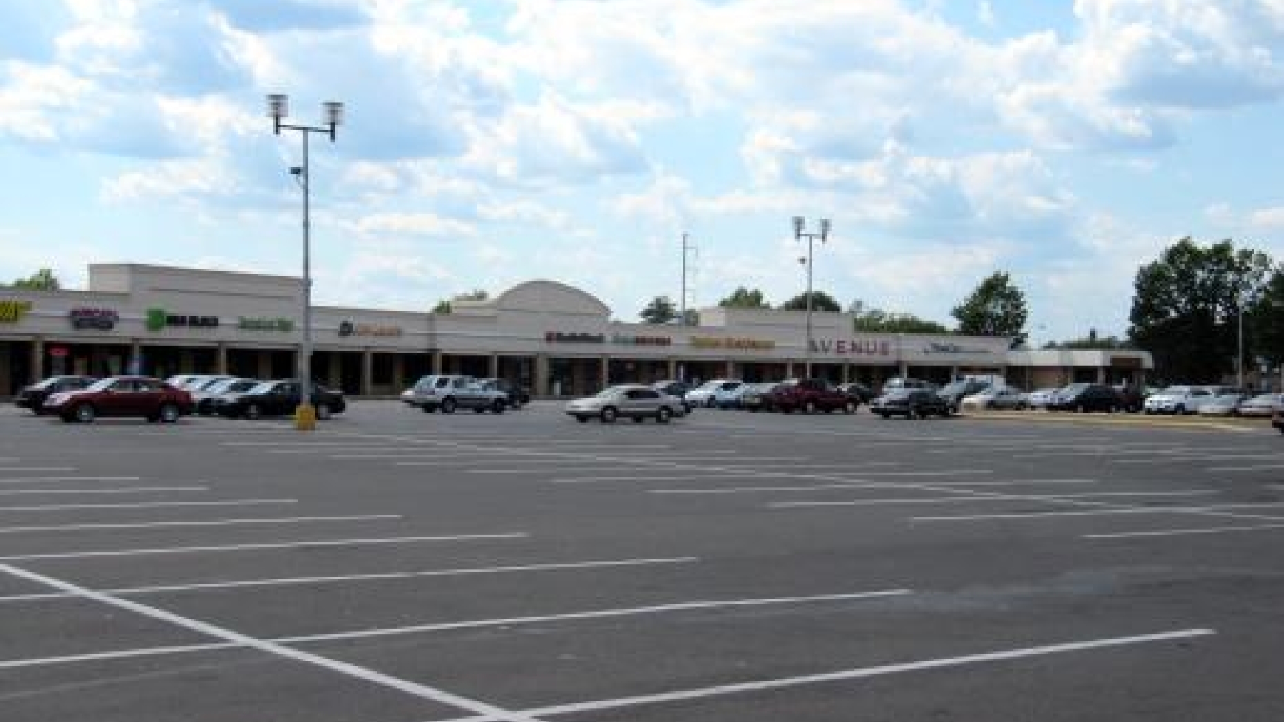 A partially filled parking lot in front of a 'strip mall' style shopping center.
