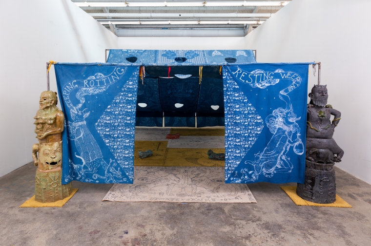 image of artwork installation, tapestry draped installation draws you into this space, two sculptures frame the entryway