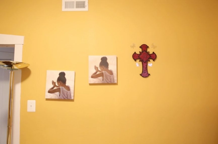A yellow wall with the same two photographs of a young girl praying and a crucifix