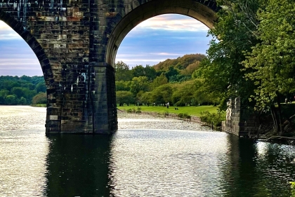 Image of the Schuylkill River Trail. Leaves changing can be seen through the arches of the bridge.