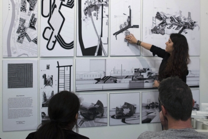 a woman pointing to large architectural drawings hung on the wall.