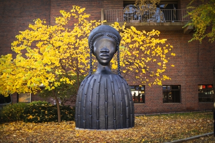 Brick House, a 16 foot bronze sculpture of an African American woman figure in front of yellow fall leaves