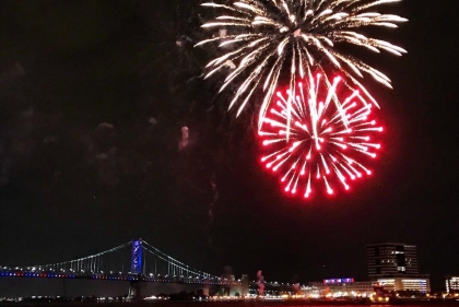 Benjamin Franklin Bridge glowing red, white and blue with fireworks above.