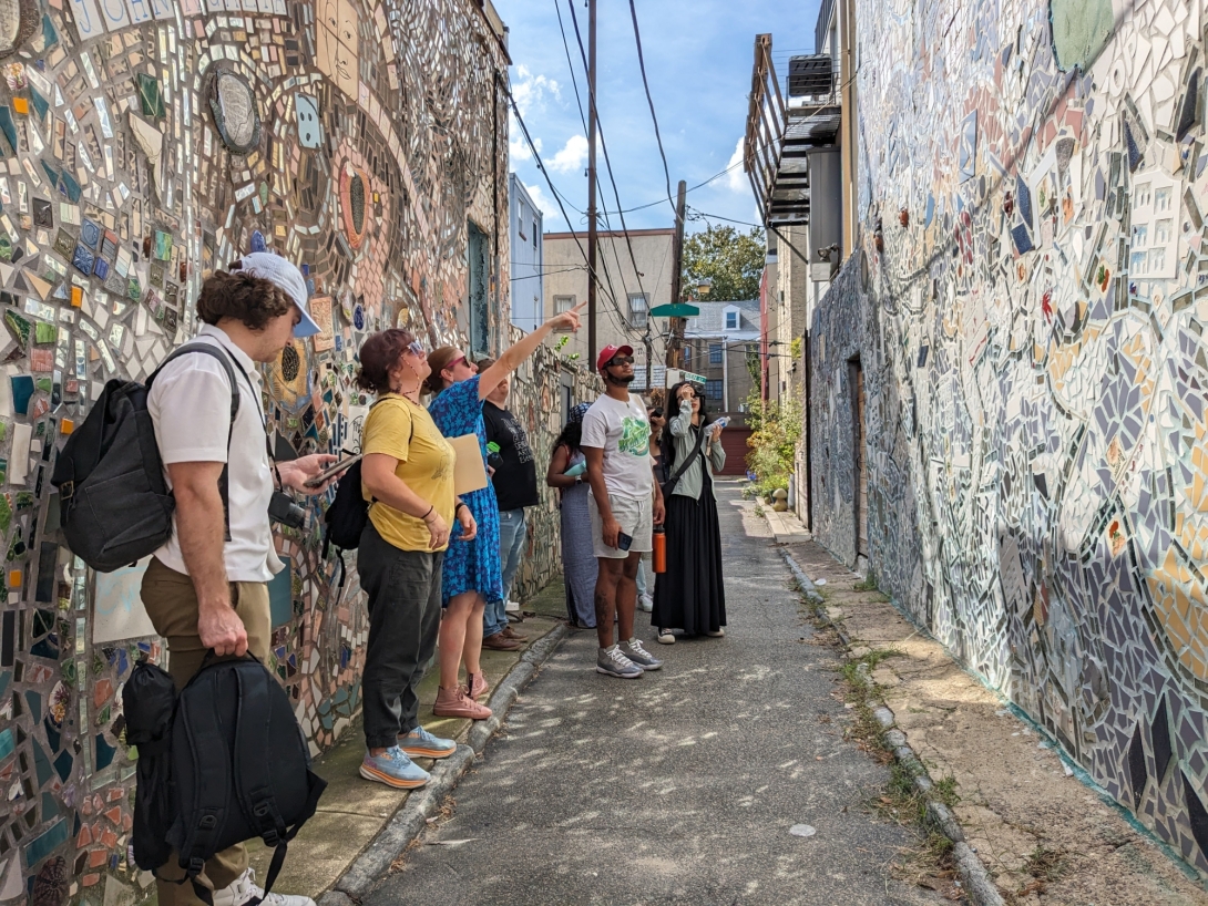 A tour group in an alleyway between mosaic murals by Isaiah Zagar