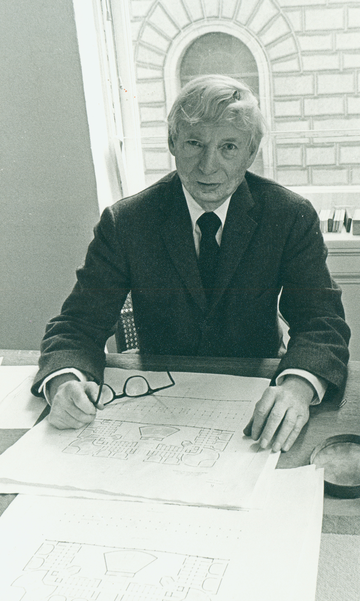 Black and white photo of Louis Kahn sitting at desk with plans in front of him