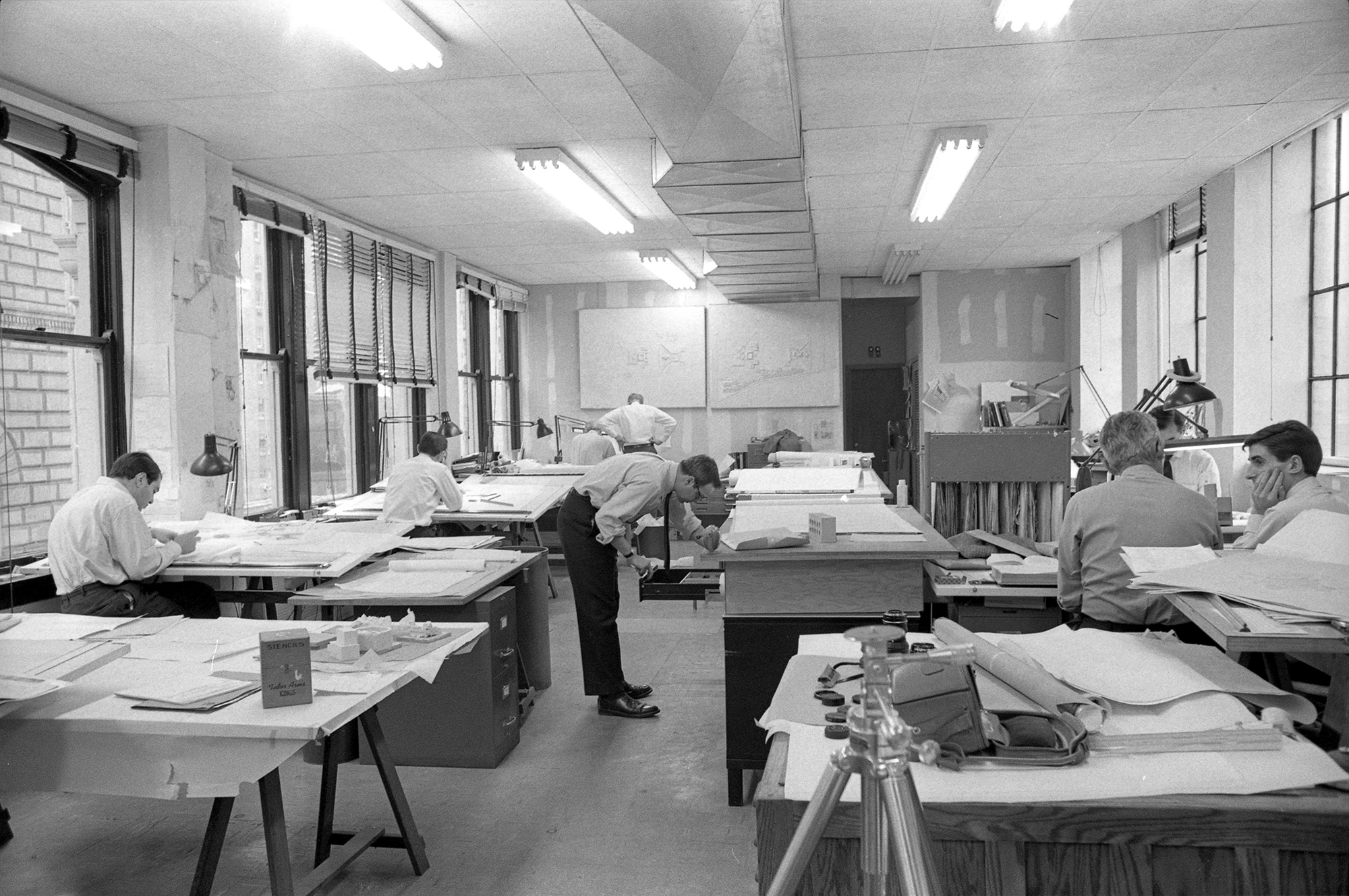 view of 1960's architecture office, with ment in white shirts working at drafting tables