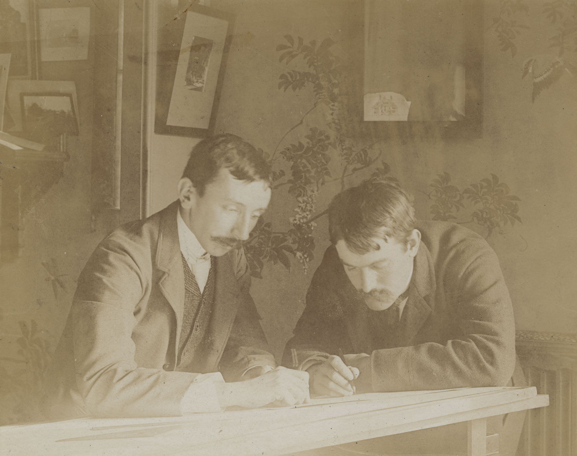 Sepia colored potrait of two male architects looking at architectural drawing