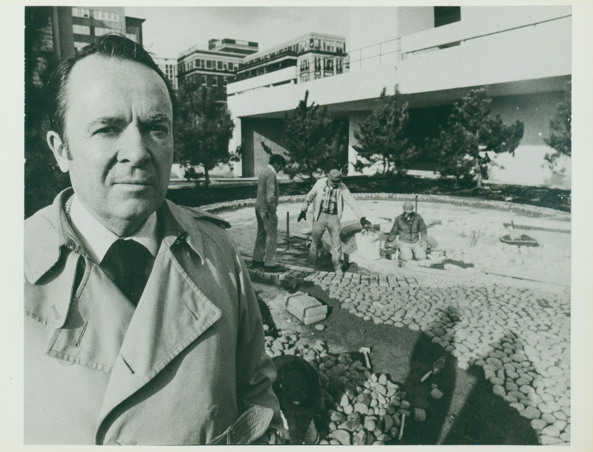 Black and white photograph of man infront of two main laying a stone courtyard