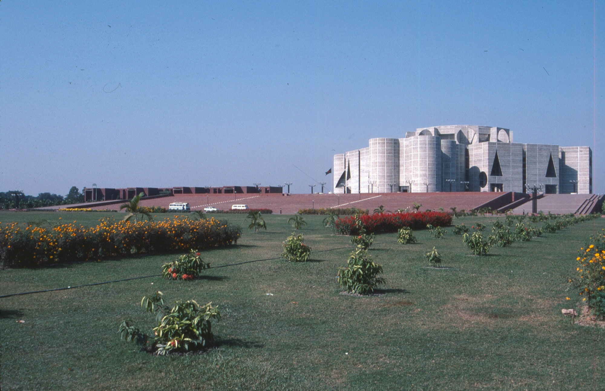 Color slide showing green grass with small plants leadning to assembly building in Bangladesh