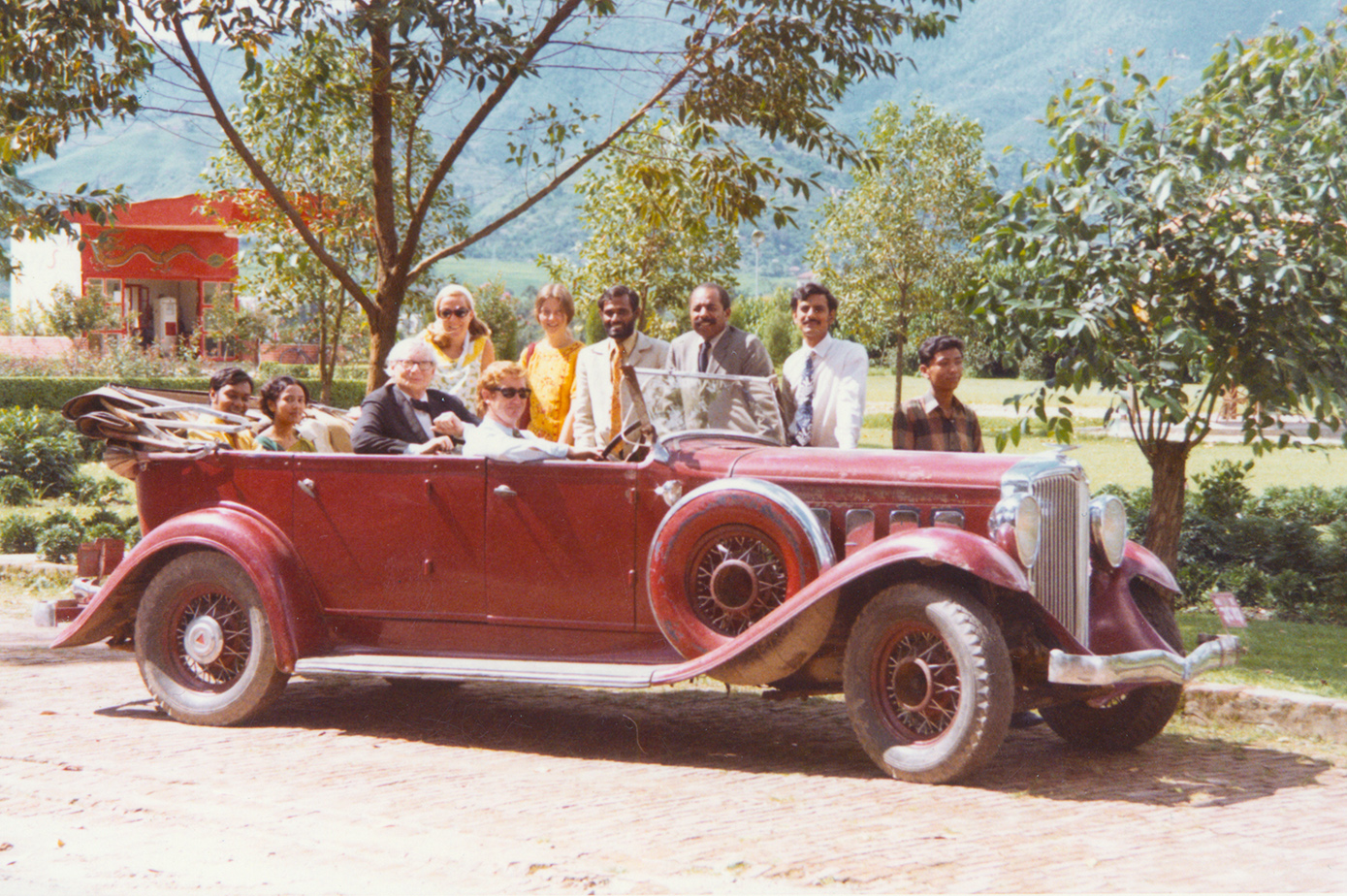 About 10 people smiling in classic red car