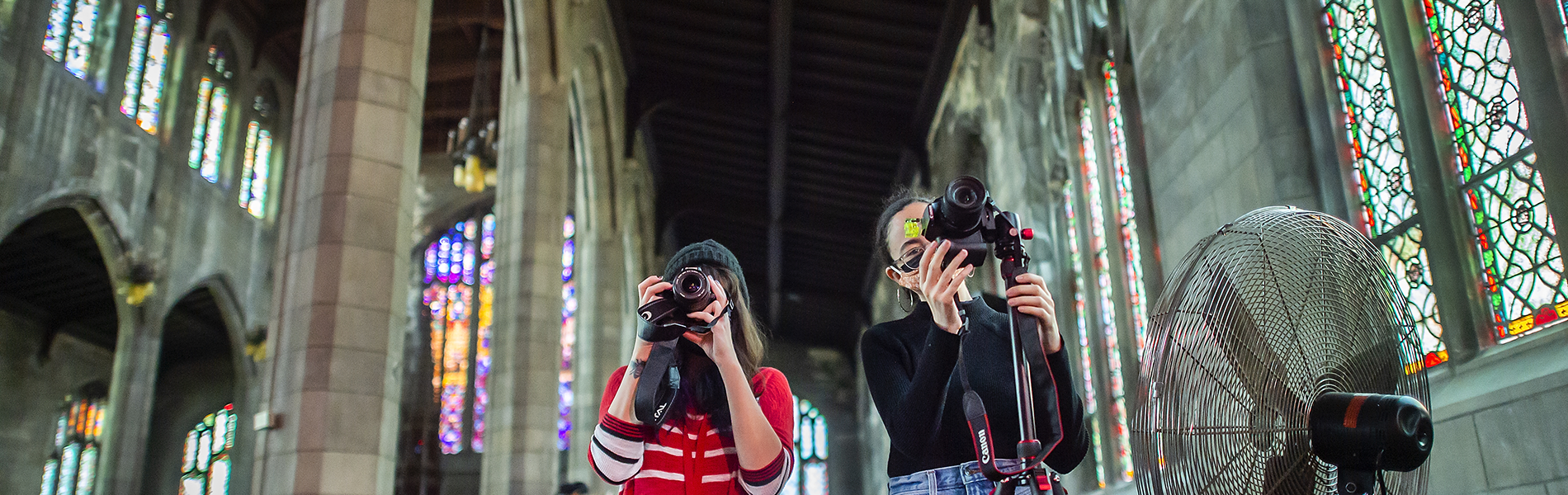  Two young women point their cameras upward inside a neo-Gothic church.