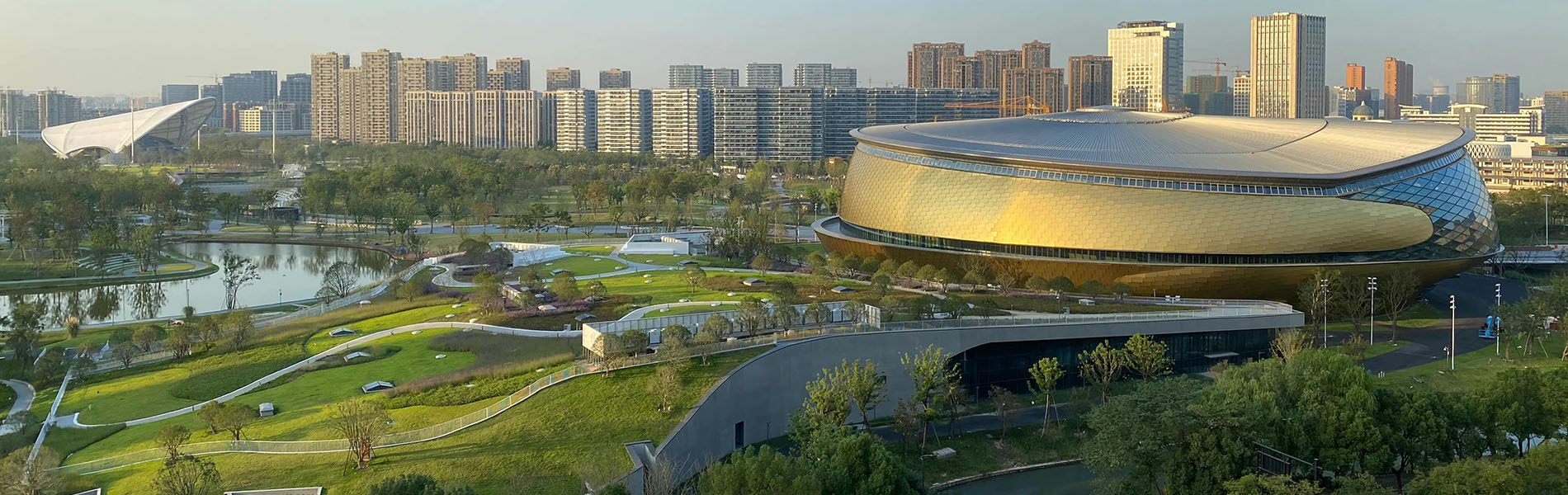 A squat saucer-like gold-clad building surrounded by grassy hills and young trees