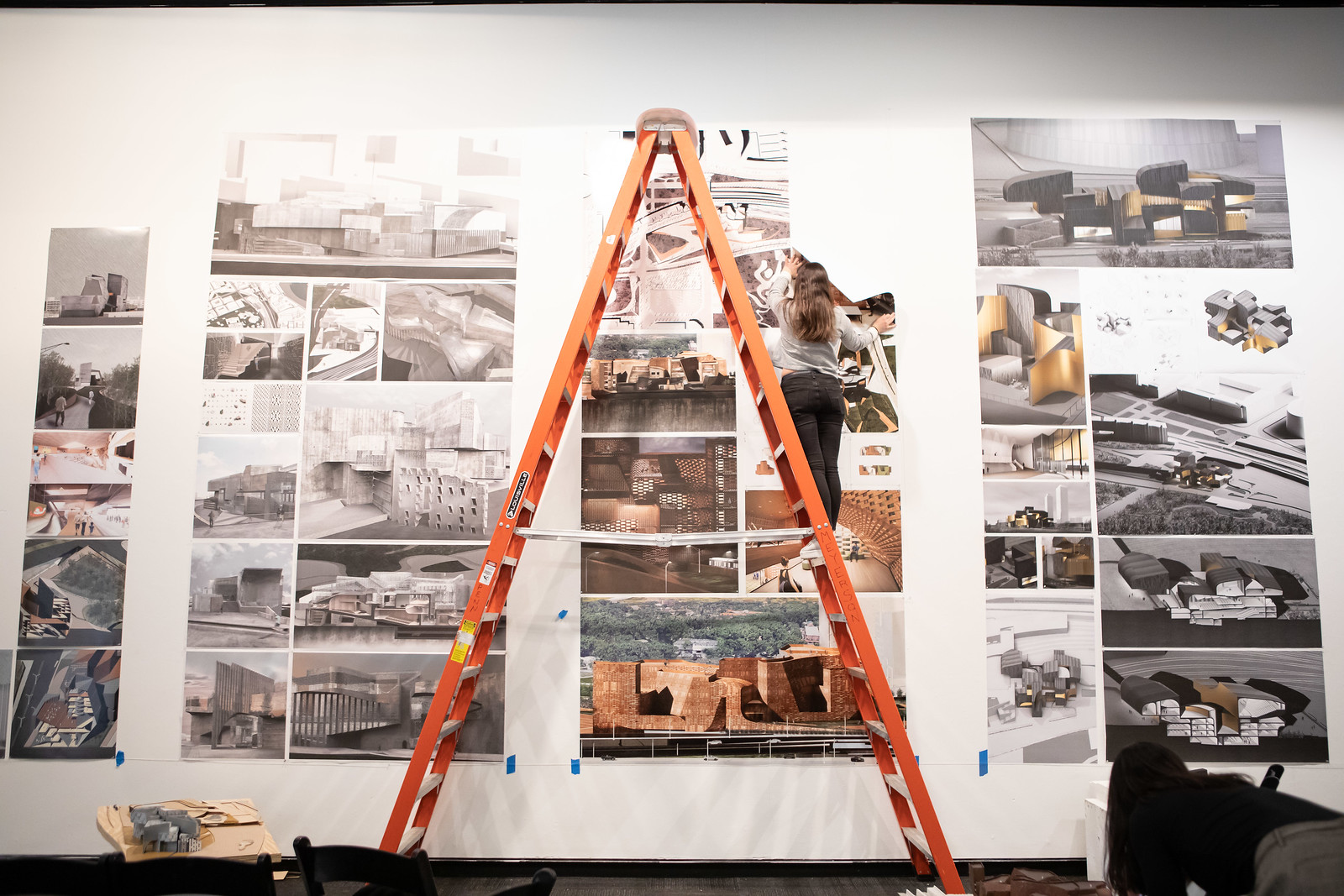 Student using a ladder to hang work on wall.