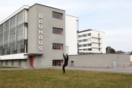 Student dancing on lawn in front of building with large sign saying "Bauhaus".