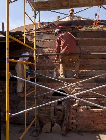 People sitting of scaffolding working on a structure made of bricks.