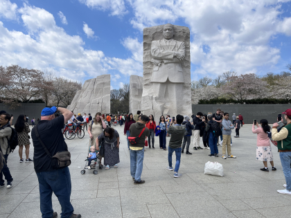 A photograph of many people standing in front of a large stone monument depicting a male figure