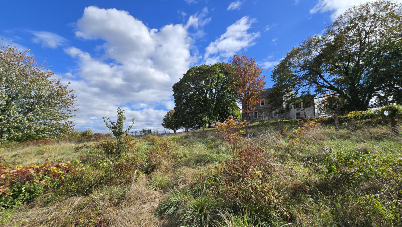 A photograph of a farm field with a stone house in the background