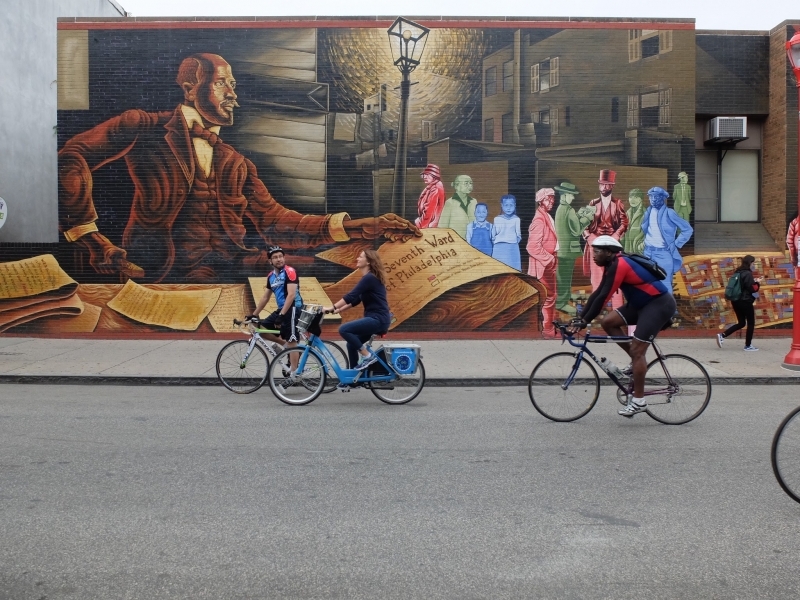People riding bicycles in front of a mural.