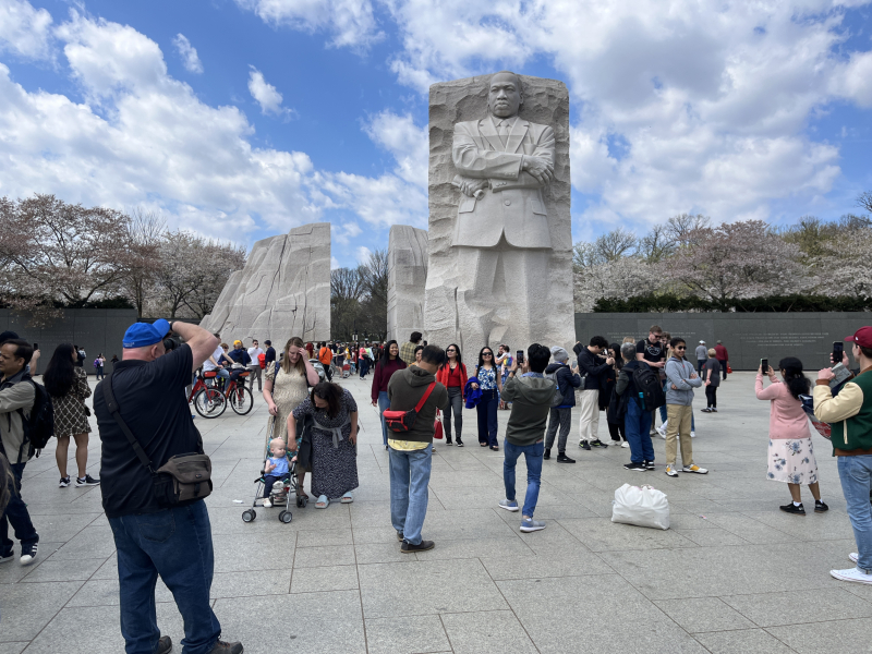 A photograph of many people standing in front of a large stone monument depicting a male figure