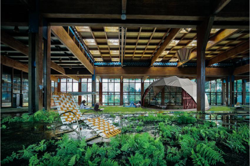 Lawn chair in foreground surrounded by lush greenery in an indoor warehouse with tent in background