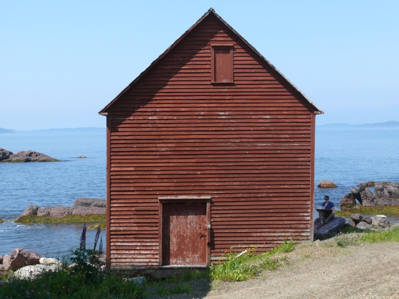 front gabled building on shoreline with rust-red paint on wood paneled facade