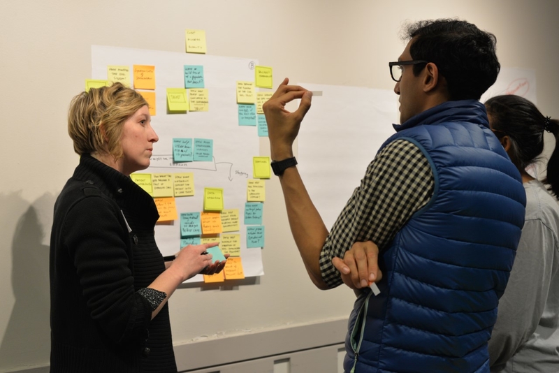 People talking next to a poster board with sticky notes all over it