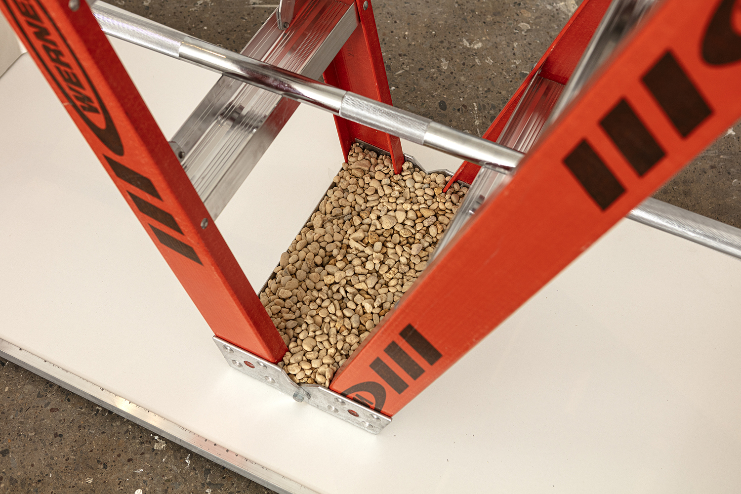 The top platform of the ladder is upside down touching the floor and has been filled with gravel