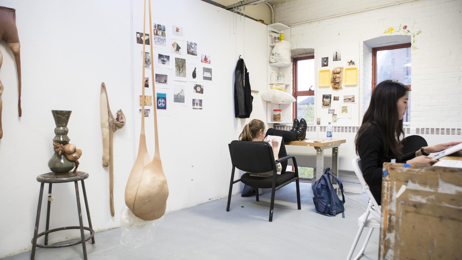 Two students working at studio tables as work hangs on the wall