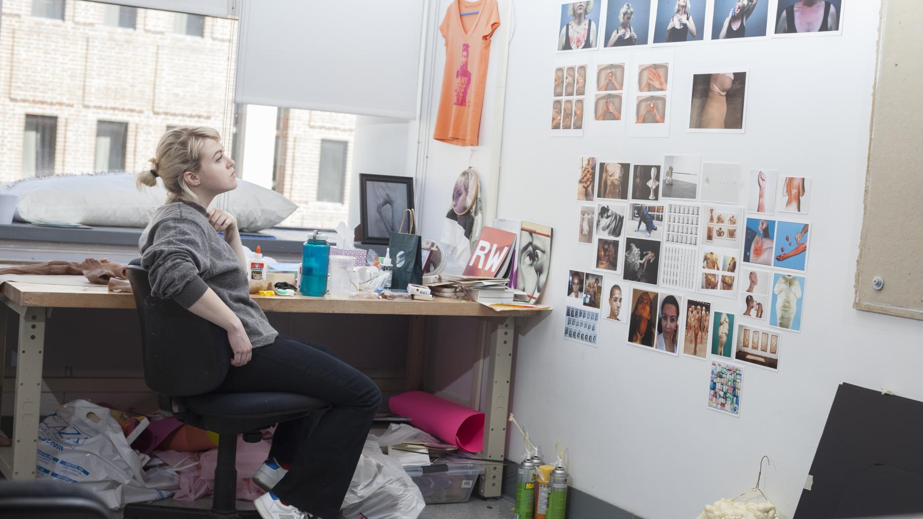 Student artist sitting at her desk viewing her art on the wall