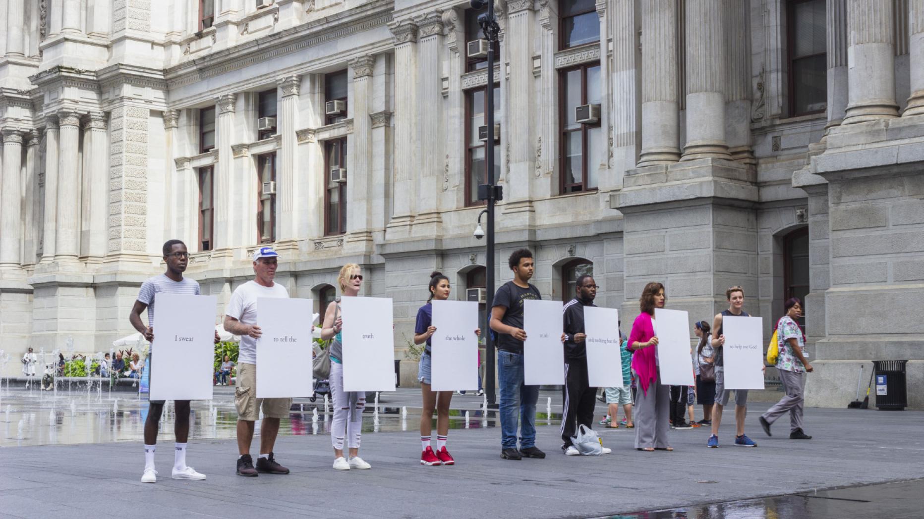 8 people standing in front of a reflecting pool, each holding a white poster board sign.