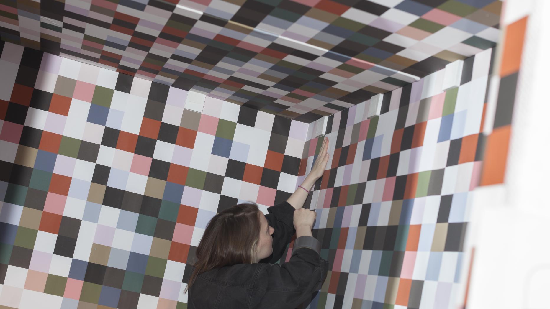 Young woman pasting on the wall, paper with squares of a variety of brown tones