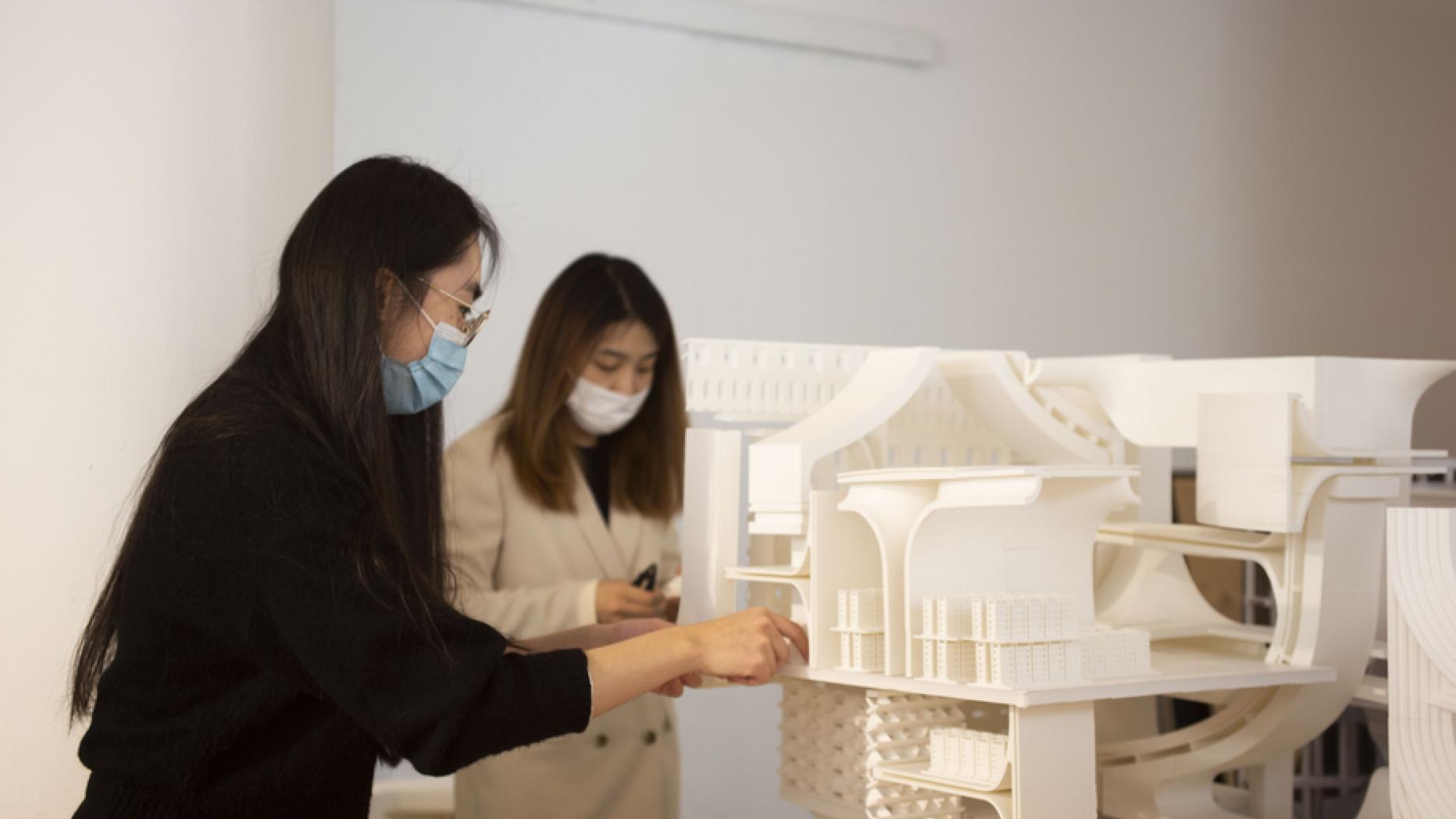 Two young women examine a white model