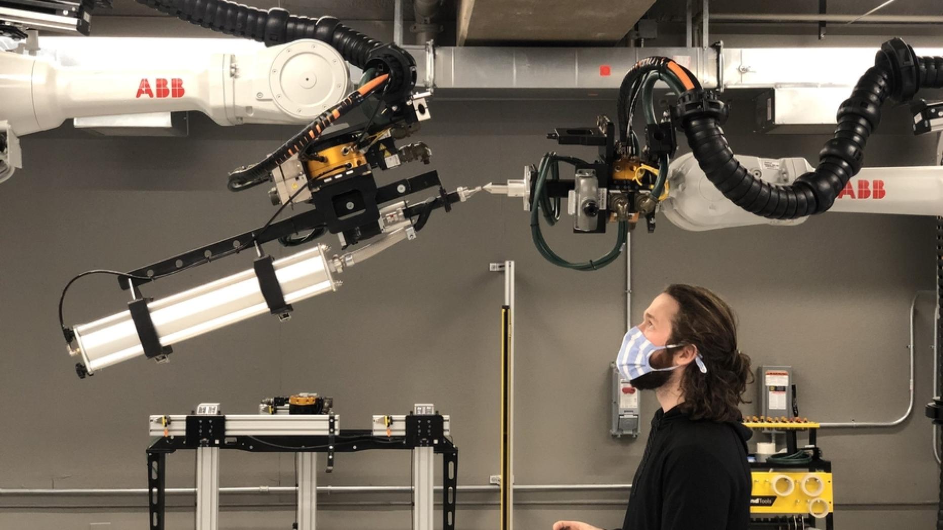 A man peers up at two robotic arms meeting overhead