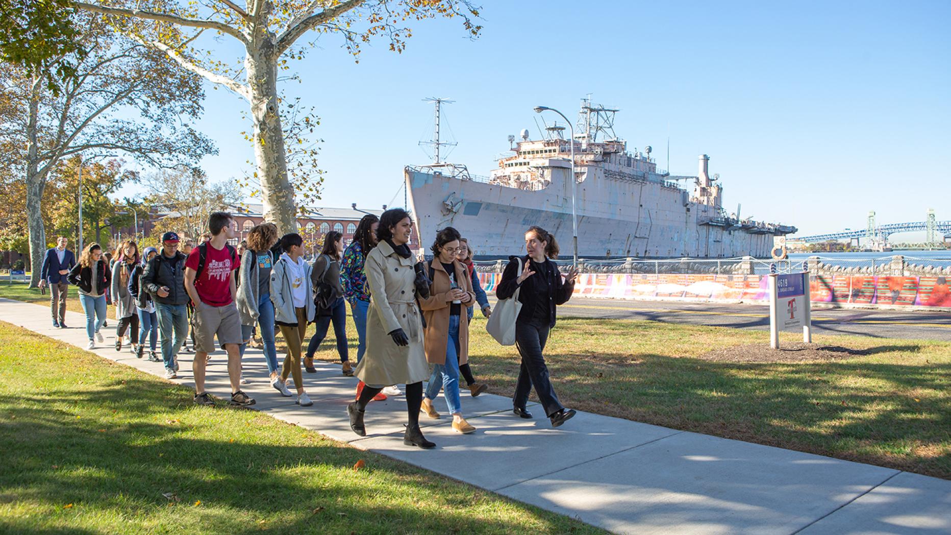 A group of people walk past a large Navy boat
