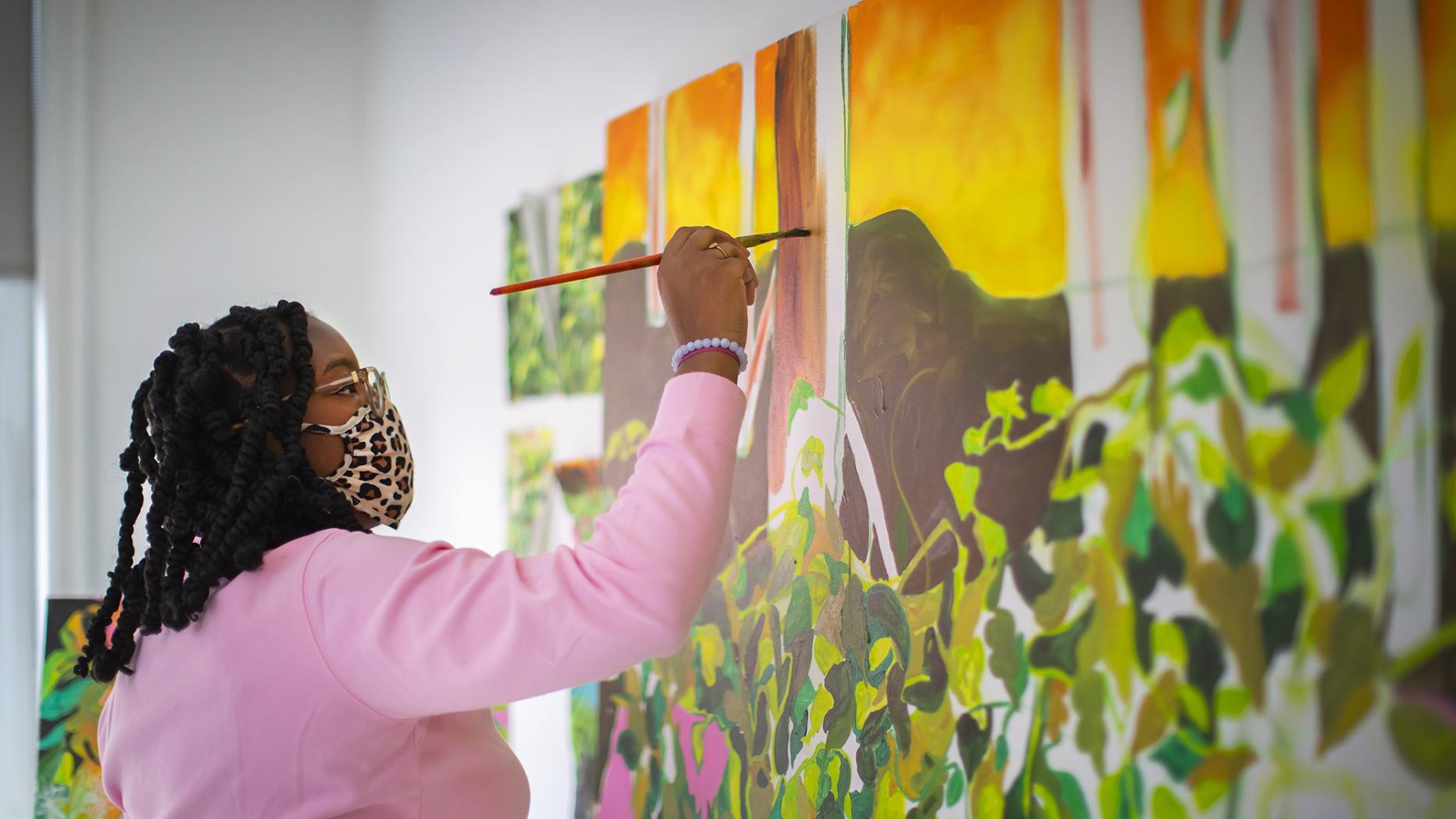 A woman in a pink sweater painting a colorful canvas
