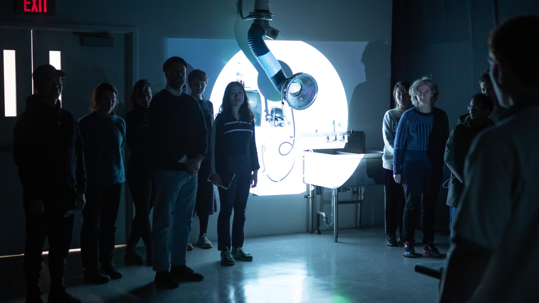 People standing in a darkened classroom with illuminated circle on wall behind them