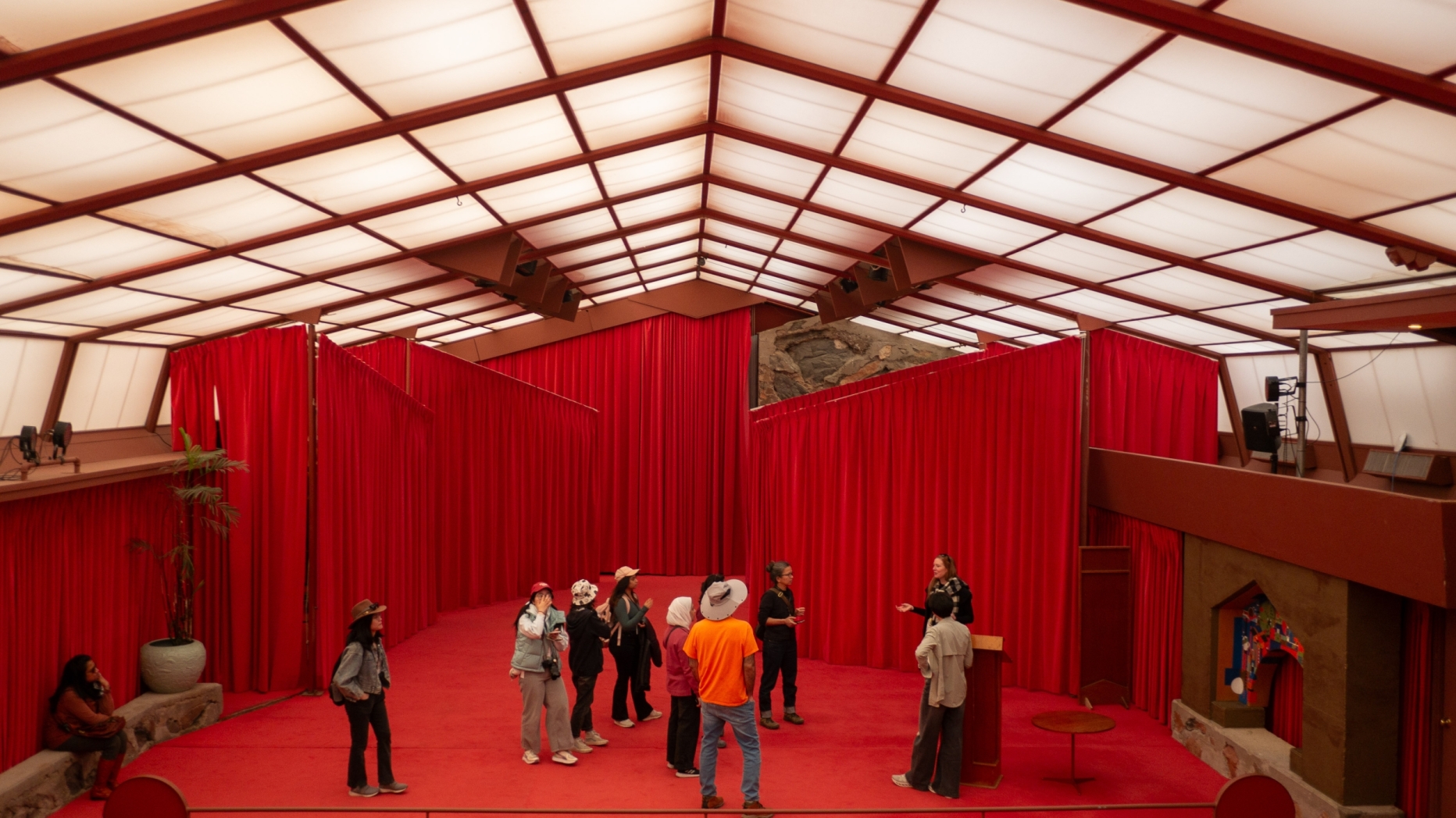 A group of people listen to a speaker while standing on the stage of the room