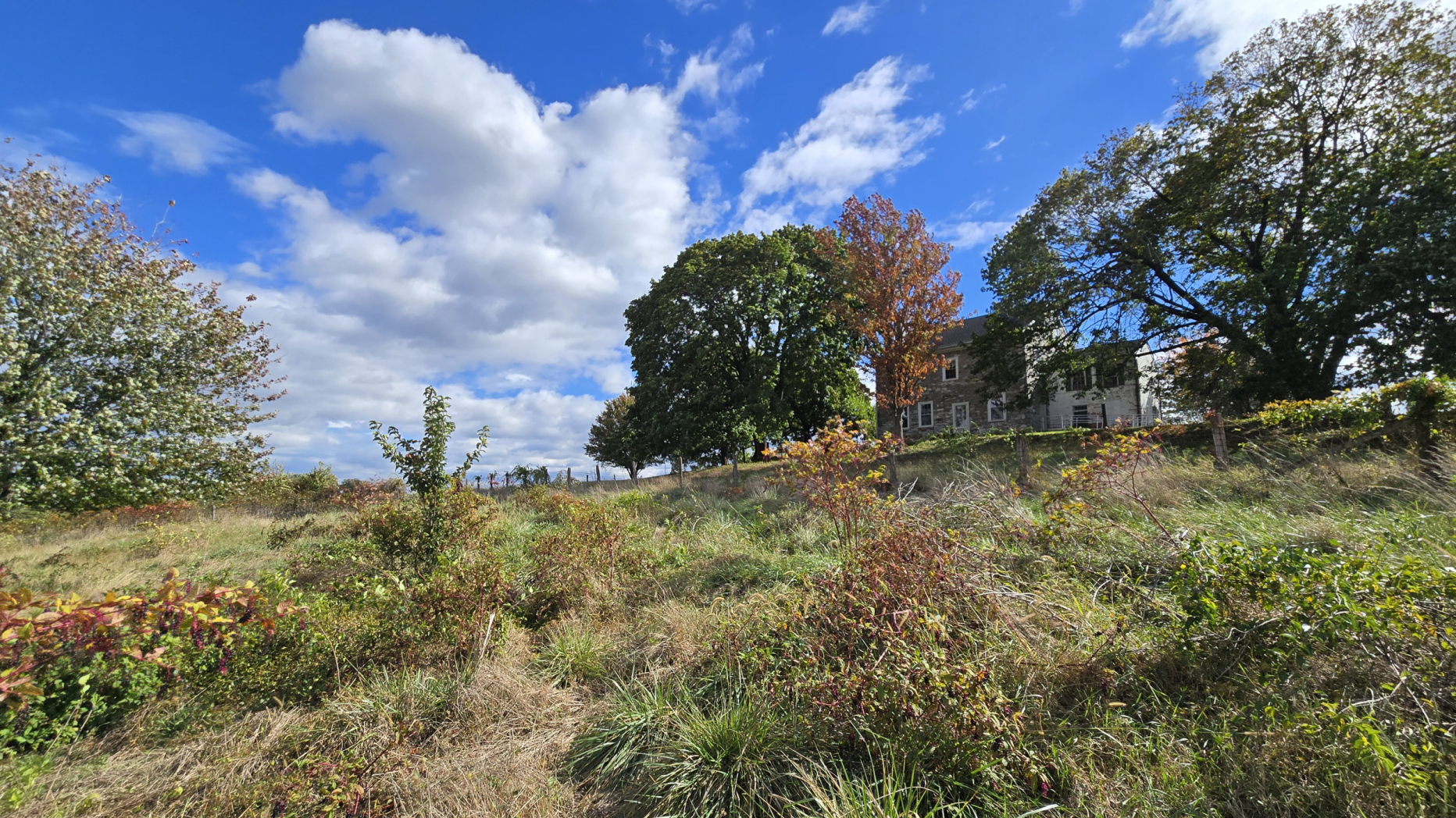 A photograph of a farm field with a stone house in the background