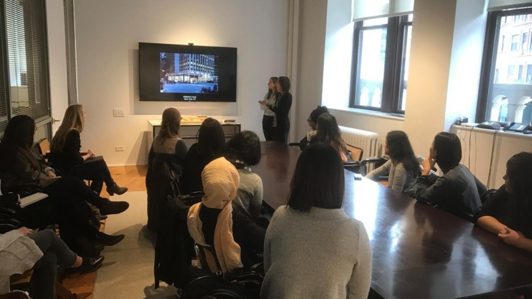 Group watching monitor display with two women giving a presentation 