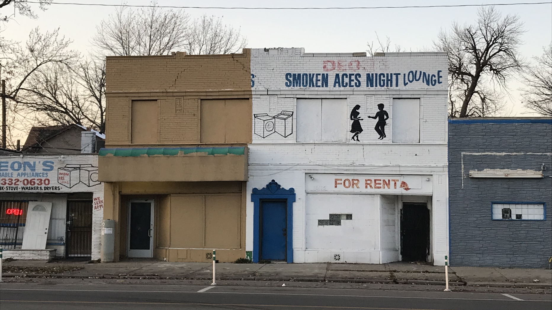  Row of abandoned storefront. One has sign that says "Smokin Aces Dance Hall" and another that says "For Rent"