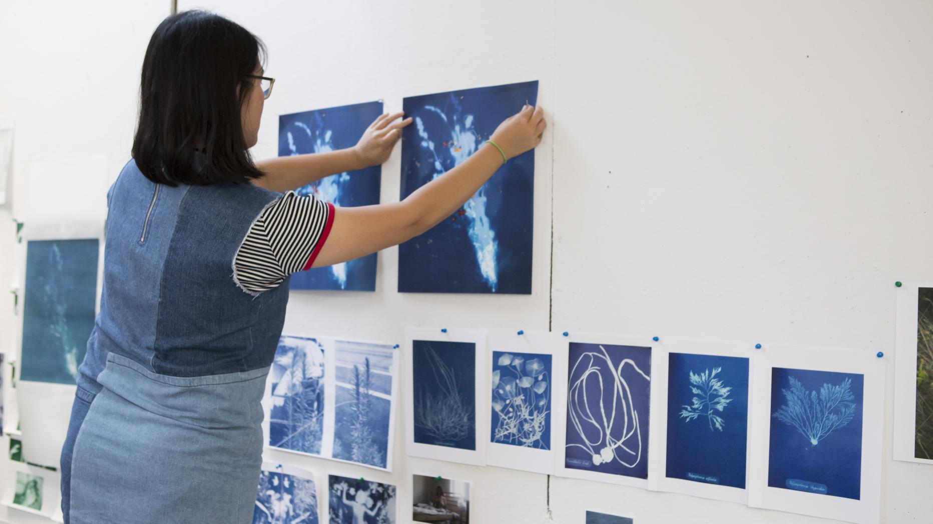 Young woman pinning blue tone photographs to a wall