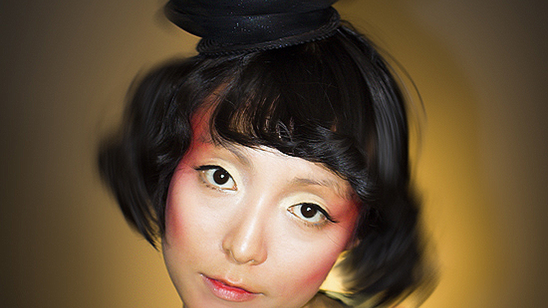Photograph of woman wearing colorful makeup and clothing. Everything outside of her face has been blurred but the colors are still visible.