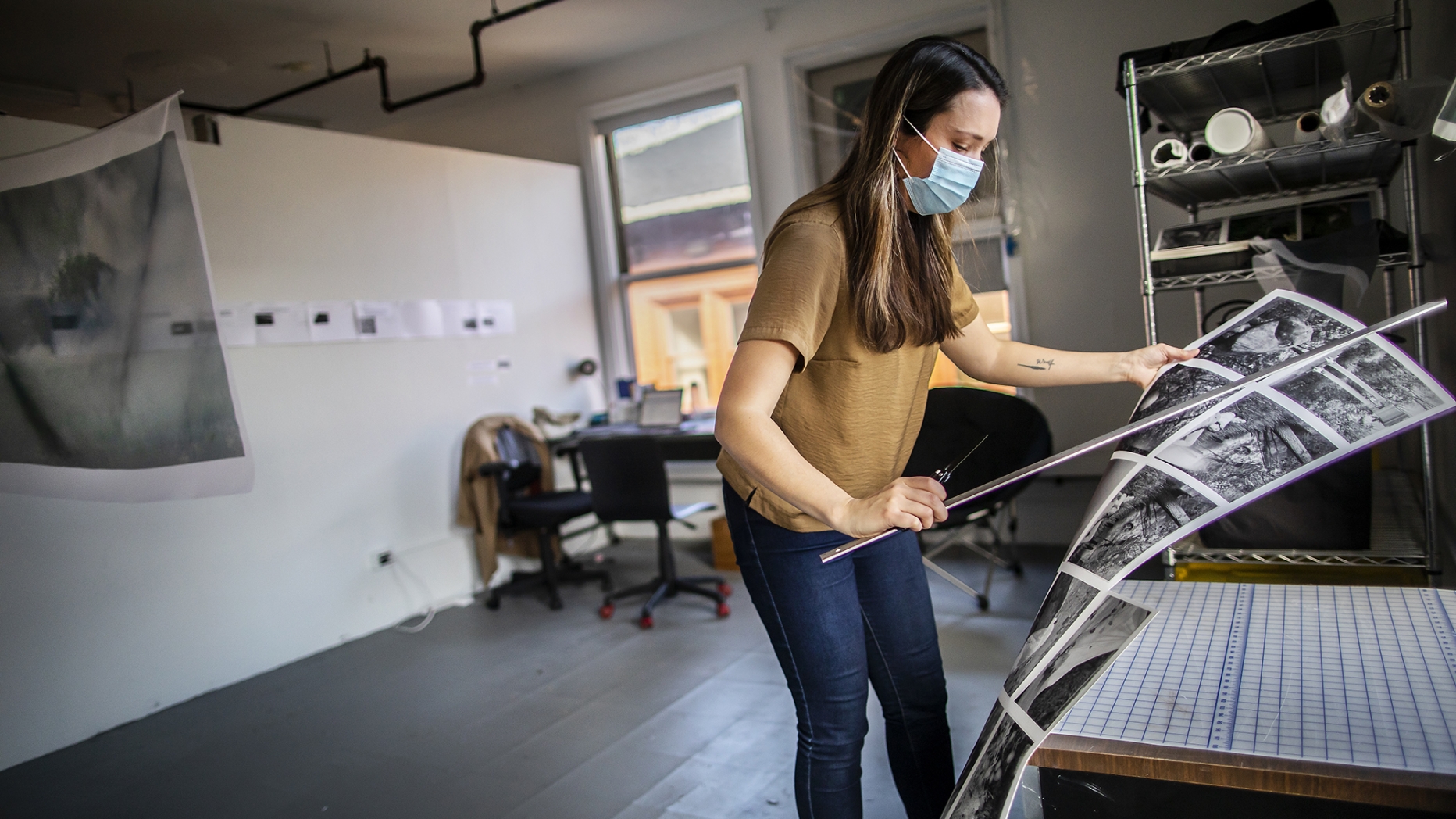 masked student moving her printed images off of a table in her studio