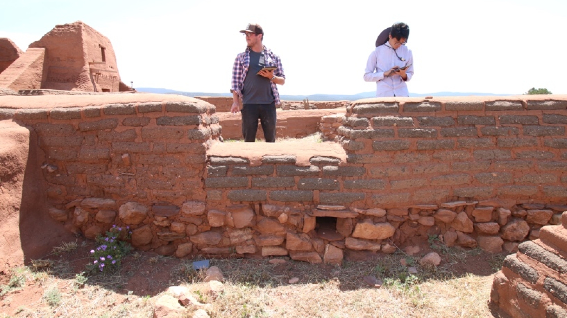 Two students survey an adobe wall.